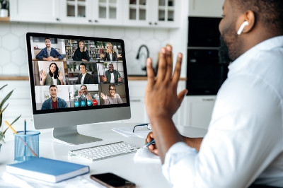 Black man seen from side. In front of him is a computer screen with six participants in a video call.