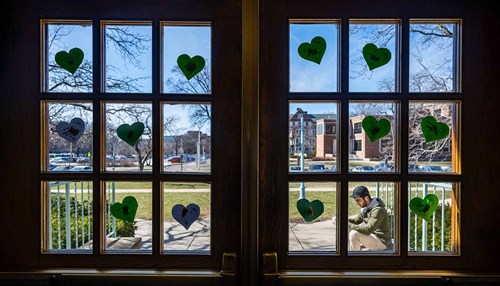 A window on an MSU campus building is covered in green paper hearts.