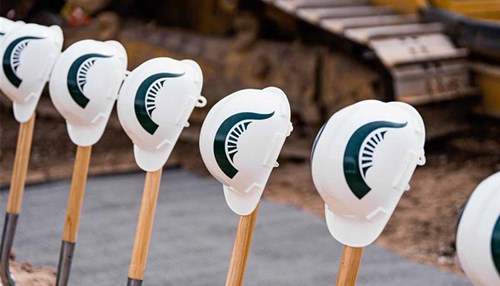 Hard hats branded with MSU Spartan plumes rest on top of shovels.